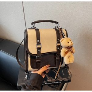 Detail view of two-tone crossbody bag with vintage metal buckles and plush bear charm