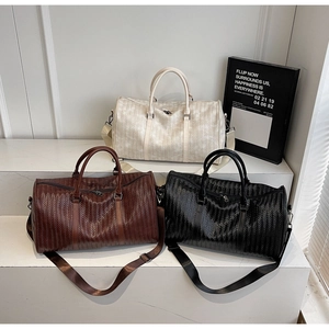 Trois grands sacs de voyage tressés en crème, marron et noir sur des supports blancs