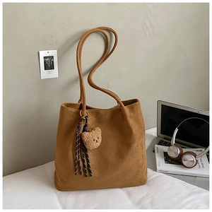 Detail view of large brown tote bag with bear charm and tassel on a cozy desk