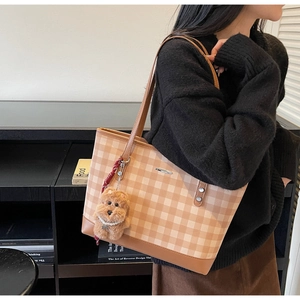 Detail view of large brown plaid tote bag with plush dog charm and leather straps