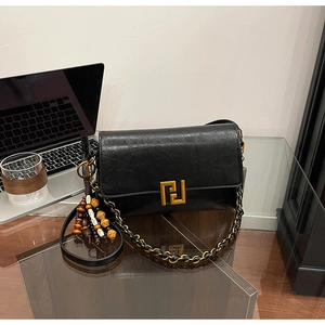 Detail of black leather crossbody bag with golden metal buckle and wood bead tassel charm
