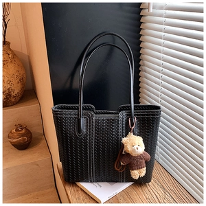 Close-up of black woven leather tote bag texture with cute bear charm and slim straps
