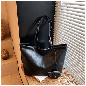 Detail of a black leather tote bag with a small glasses pouch on a wooden table