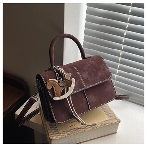 Detail of burgundy matte flap bag with contrast stitching and leather pony charm