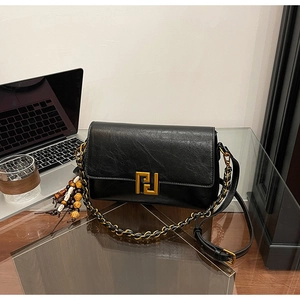 Detail of vintage black leather shoulder bag with gold geometric buckle and chain strap