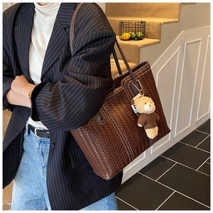Detail of dark brown woven tote bag featuring contrast stitching and a cute bear charm