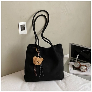 Detail of a black canvas tote bag with a cute brown teddy bear charm on a bed