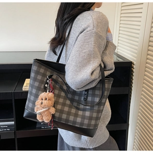 Detail of grey plaid tote bag featuring a cute brown teddy bear plush charm and slim handles