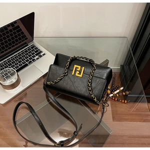 Detail of vintage black leather bag featuring gold logo and wooden bead tassel accessory