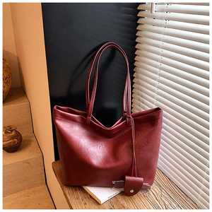 Close-up of wine red faux leather tote bag showing lychee grain texture and side pendant