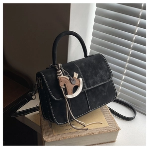 Detail of black suede bag featuring contrast white stitching and wooden horse charm