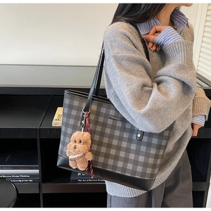 Detailed view of checkered tote bag with plush bear charm worn on shoulder