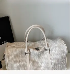 Détail du sac de voyage crème montrant la texture tissée et les attaches en métal gris mat
