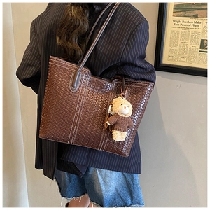 Detail of dark brown woven tote bag with cute bear charm worn on shoulder