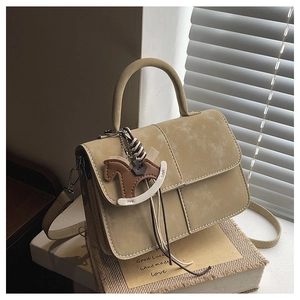 Detail of khaki leather crossbody bag with flap closure and decorative horse pendant