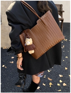Close-up of a brown woven tote bag with a cute bear charm and white contrast stitching