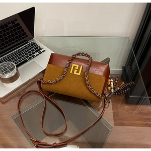Detail of a brown leather shoulder bag with a gold buckle and bead charm on an office desk
