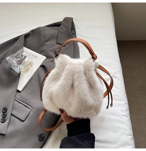 Detail of white faux fur bucket bag featuring brown leather handle and drawstring closure
