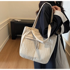 Detailansicht der beigen gesteppten Tragetasche mit Seitentasche und gewebtem Knoten-Zipper