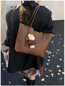 Detail of a brown woven tote bag with a small bear charm held by a model in autumn