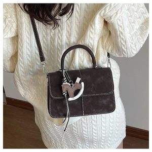 Detail of dark brown retro handbag with white stitching and stylish horse charm