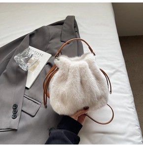 Close-up of white plush bucket bag featuring brown faux leather drawstring and strap details