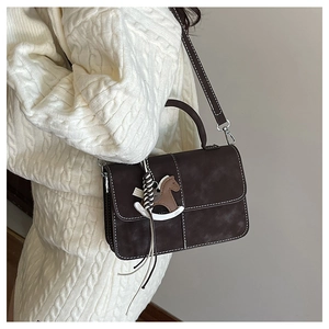 Detail of dark brown retro shoulder bag with white contrast stitching and horse charm