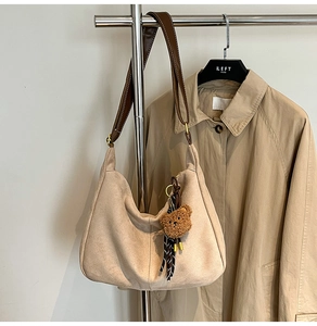 Dettaglio della borsa tote beige con tracolla in pelle marrone e ciondolo a orsetto