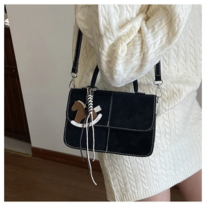 Detail view of black vintage crossbody bag with white contrast stitching and a horse charm