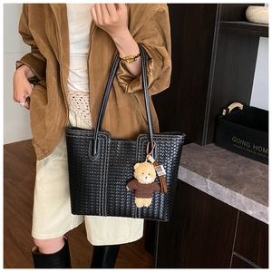 Detail of black woven tote bag with white stitching and cute plush bear charm accessory