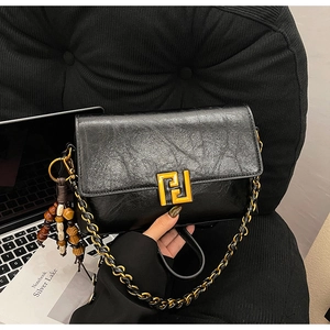 Detail of black wax-leather crossbody bag with gold F-buckle and beaded tassel