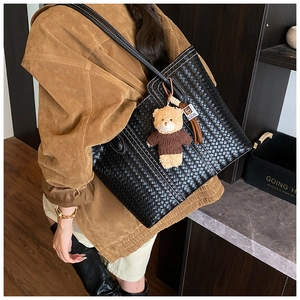 Detail of black woven leather tote bag with brown bear charm and white stitching