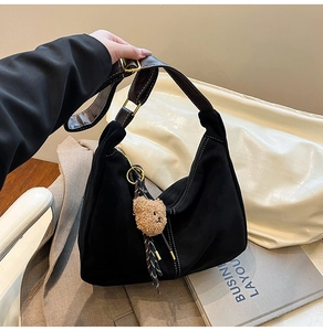 Dettaglio della borsa hobo in pelle scamosciata nera con tracolla marrone e ciondolo orsetto