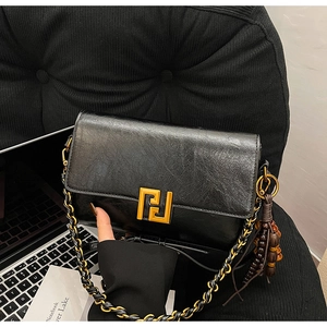 Detail of black crossbody bag featuring a golden geometric lock and leather chain strap