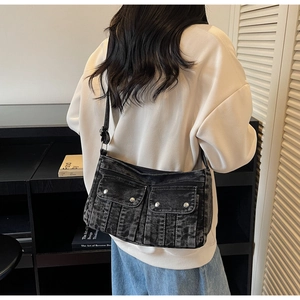 Side view of a washed denim crossbody bag with silver rivets worn by a model in a studio