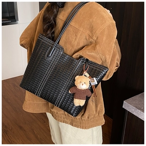 Detail of black woven tote bag with white contrast stitching and a small teddy bear charm