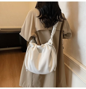 Detail einer weißen Cord-Schultertasche mit plissiertem Trageriemen auf khakifarbenem Mantel