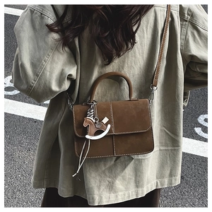 Close-up of brown suede mini square bag with contrast stitching and horse charm