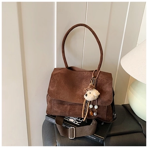 Detail of deep brown suede crossbody bag with plush bear charm in cozy room setting