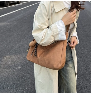 Vista esterna di una borsa hobo in pelle scamosciata marrone con pompon e dettagli cinturino