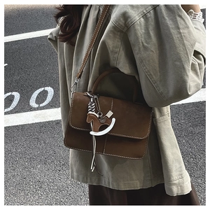 Detail of a brown suede small crossbody bag with a unique rocking horse charm accessory