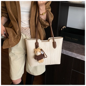 Detail of woven cream tote bag with dark brown leather handles and cute bear charm