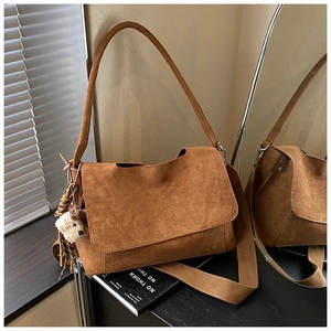 Detail of a brown suede shoulder bag featuring a wide fabric strap and bear charm
