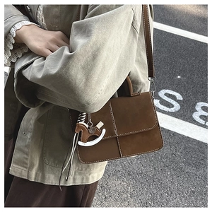 Detail of a brown suede crossbody bag with white stitching and a horse-shaped charm pendant