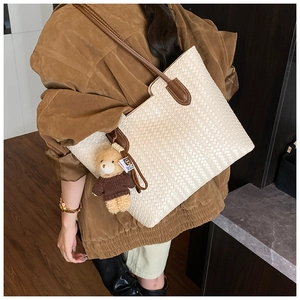 Detailed view of beige woven tote bag with brown leather straps and a bear pendant
