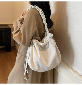 Detailstruktur der beigen Cord-Schultertasche mit gerafftem Träger am Modell