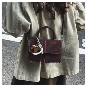 Close-up of a dark brown suede crossbody bag with white stitching and a horse charm