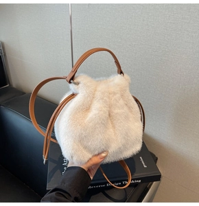 Close-up of cream faux fur bucket bag with brown leather handle and drawstring detail