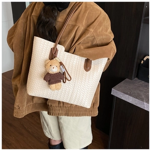 Detail of a woven cream tote bag with brown straps and a cute plush bear charm