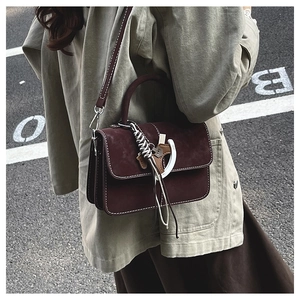 Close-up of vintage burgundy suede crossbody bag with contrast stitching and horse pendant